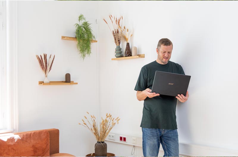 Coach Josef Mayer lehnt an einer weißen Wand mit Laptop in der Hand