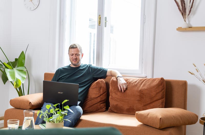 Single Coach Josef Mayer sitzt mit Laptop auf einer orangen Couch