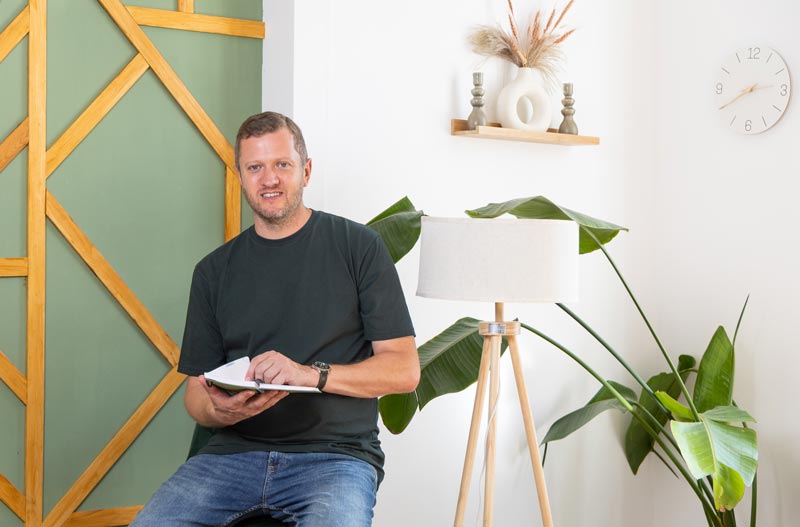 Jugendcoach Josef Mayer sitzt mit einem Block in der Hand vor einer grünen Wand